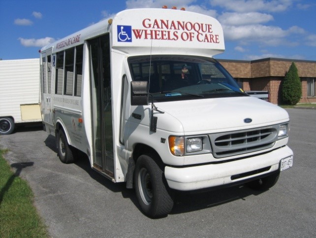 A picture of a short white bus, with the words Gananoque Wheels of Care across the top.